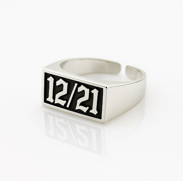 Silver ring with a black rectangular face displaying '12/21' on a white background